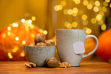 Celebrating autumn evening with cup of hot tea, pumpkins and walnuts closeup - teabag with white...