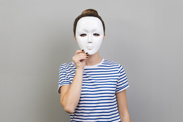 Portrait of unknown anonymous woman wearing striped T-shirt covering her face with white mask,...