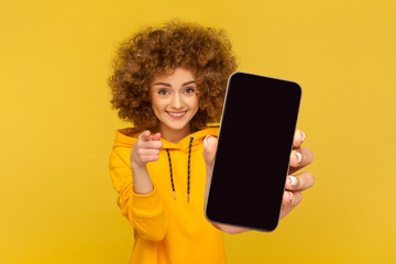 Portrait of attractive smiling woman with Afro hairstyle wearing hoodie showing big mobile display...