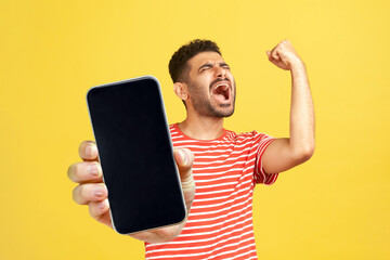 Extremely happy joyful man with beard wearing red T-shirt standing showing big mobile phone with...