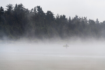 Surfer carrying surf board in the mist, Chesterman Beach, Tofino, Vancouver Island, Canada.