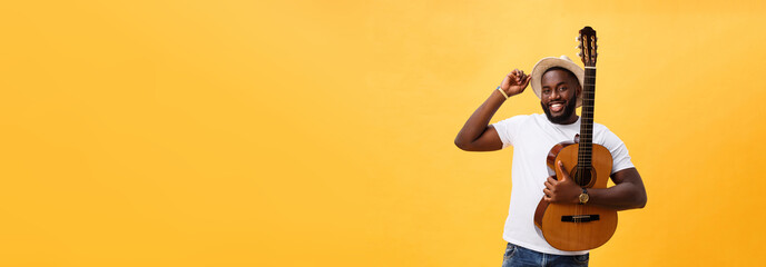 Muscular black man playing guitar, wearing jeans and white tank-top. Isolate over yellow background.