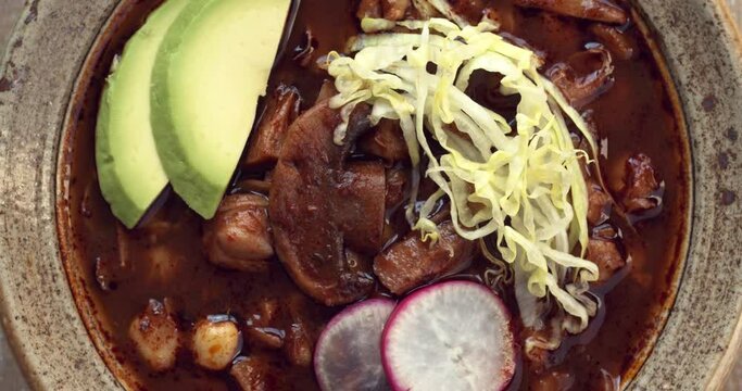 Pozole Rojo with with cacahuazintle, shredded jackfruit, mushrooms and dried chilies. Vegan traditional style Mexican dish close-up.
