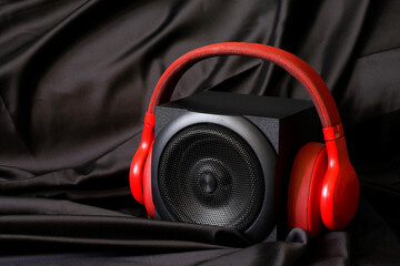 Black wooden audio speaker with a metal grill and red wireless headphones in a natural silk...
