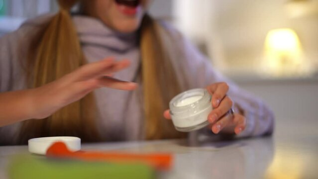 Teenage female hands opening cosmetics jar applying moisturizer on palms. Unrecognizable Caucasian teen girl taking care of skin sitting at home indoors. Beauty routine and lifestyle concept