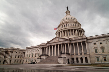 The east side of the United States Capitol Building in Washington, D.C. seen on a winter afternoon. The sky is filled with grey clouds while the plaza is devoid of people. Low angle wide shot.