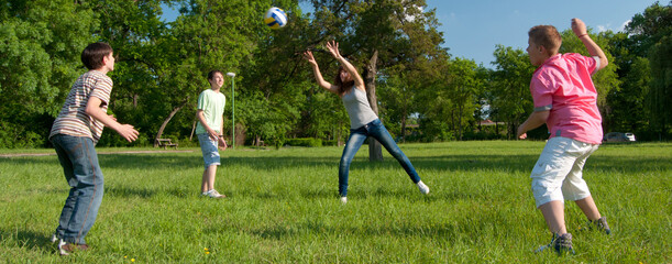 Teenagers boys and girls playing volleyball in the park on sunny spring day - 535362292