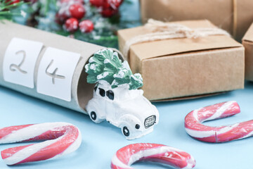 Toy car with Christmas tree, toilet paper tube with number 24, lollipops and handmade gifts with fir branches on a blue background.
