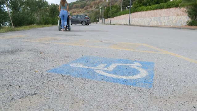 Invalid parking sign with woman caregiver walking with paraplegic disabled boy on wheelchair on outdoor scenery,healthcare 