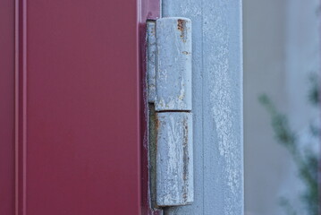 one iron old gray door hinge in rust on a metal gate on a  red wall in the street