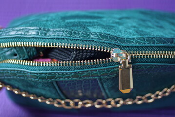 one open yellow metal zip on a green leather bag on a purple background