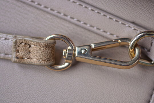 one yellow metal latch with a ring on the strap of a brown leather bag