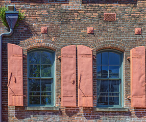 Fototapeta na wymiar Vintage Brick Building from 1800 with Arched Windows and Pink Metal Hurricane Shutters.