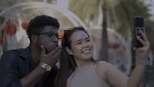 Close up of multirace couple using smartphone to take a picture. Goofy boyfriend makes girl laugh 