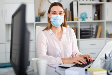 Fototapeta na wymiar Businesswoman in personal protective equipment working on laptop in office