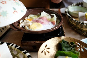 Japanese hot pot (nabe) with cabbage, enoki mushrooms, bacon, a poached egg as part of a...