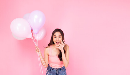 Excited cheerful asian woman holding balloons and hands beside mouth smiling with toothy standing over isolated pink background. Joyful teenager girl with pastel balloons shocked  amazed expression.