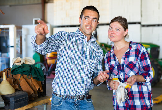 Two farm workers colleagues working in greenhouse. Experienced man showing what and where to young woman