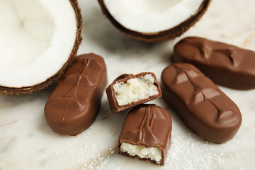 Delicious milk chocolate candy bars with coconut filling on white table, closeup