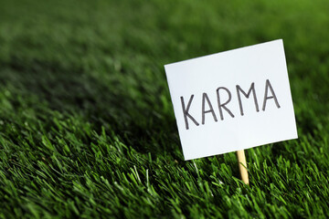 Sign with word Karma on green grass, closeup. Space for text