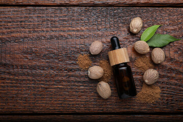 Fototapeta na wymiar Bottle of nutmeg oil, nuts and powder on wooden table, flat lay. Space for text