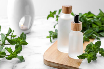 Bottles of mint essential oil and fresh leaves on white marble table