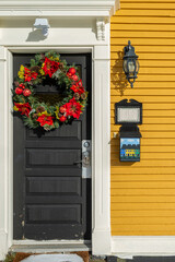 A black colored door with a vibrant Christmas red wreath covered in poinsettia flowers hung on the...