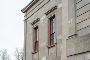 The exterior of a vintage limestone block wall with multiple windows. The tall government building...