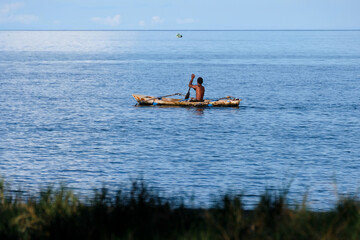 A Timorese fisherman paddling a traditional wooden fishing canoe boat over calm placid ocean water on tropical island in Timor Leste, Southeast Asia