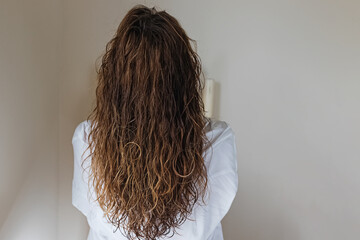 Brunette woman with long wavy hair, view from the back. Styling with curly method