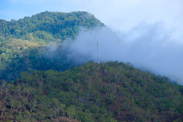 Clouds lingering at the tree covered mountain tops with a telecommunications tower on the off the beaten path, rugged, remote and tropical Atauro Island in Timor Leste, South East Asia