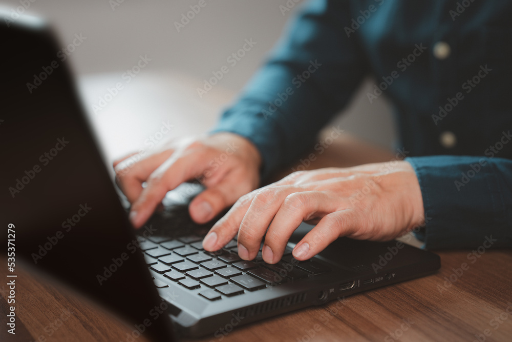 Poster Closeup image of a young man working and typing on laptop computer keyboard on wooden table in cafe.