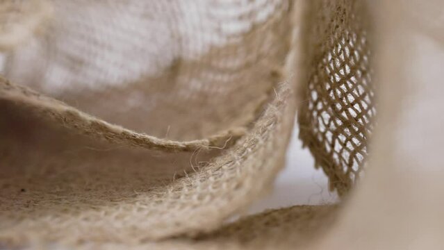 Sliding in front of loose hemp fabric on white background with selective focus creating background footage with texture and textile curves