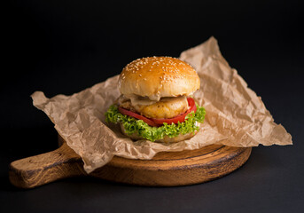 Close-up of a delicious fresh homemade burger with lettuce, cheese, onion and tomato on a rustic wooden board on a dark background