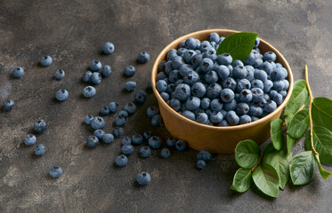 Freshly picked blueberries in a wooden bowl on a wooden background. Healthy food and nutrition.