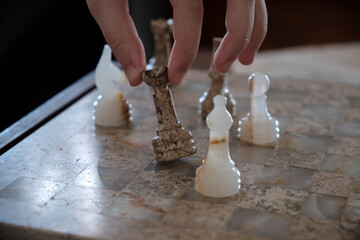 Chess piece being moved by a delicate hand. Cropped fingers picking up a queen chess piece carved...