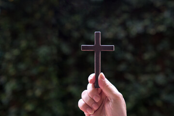 Hand holding a wooden cross crucifix with nature background. Concept for Christian faith and Good Friday.