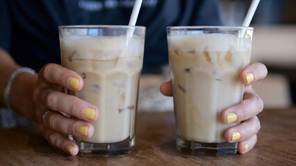 Women's hands with bright manicure slowly move two glasses filled with a cocktail along the surface of a wooden table to the center directly at the camera.