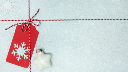 red gift tag with christmas star, red white twine rope with bow. festive silver background.
