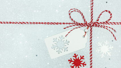 red white twine rope and bow with gift tag and snowflakes on silver background with star confetti