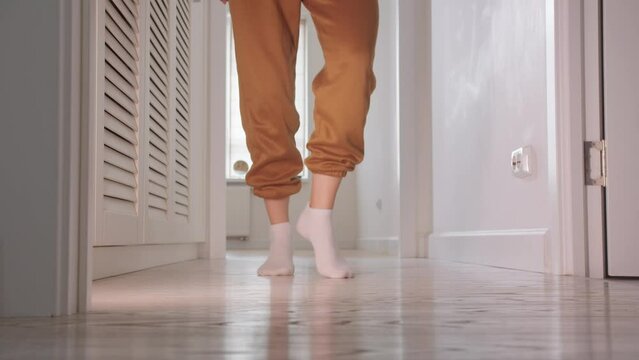 A young woman in white socks dances in the bright corridor of her flat