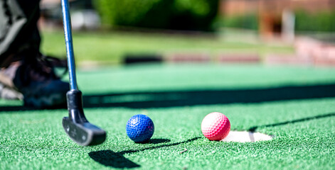 Mini golf game with several colored balls in the way of a putter lined up.