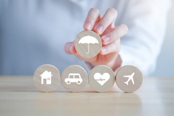 Insurance concept. Protection against a possible eventuality. Hand holding umbrella icon for security symbol and House, Car, Health care and travel icon on wooden circle for assurance life concept.