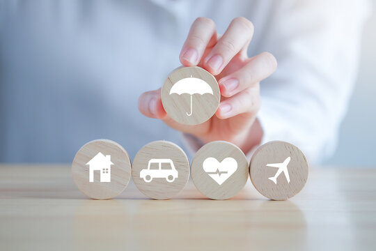Insurance concept. Protection against a possible eventuality. Hand holding umbrella icon for security symbol and House, Car, Health care and travel icon on wooden circle for assurance life concept.