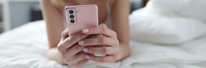 Young woman lying on bed and holding mobile phone in her hands closeup