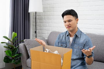 Disappointed  Asian guy with cardboard parcel with order from internet online store, copy space