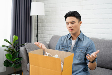 Asian man dissatisfied by received parcel, unhappy customer unpacking cardboard box, wrong online...