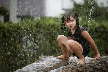 Cheerful child girl playing on heap of wet soil during raining in rainy season.