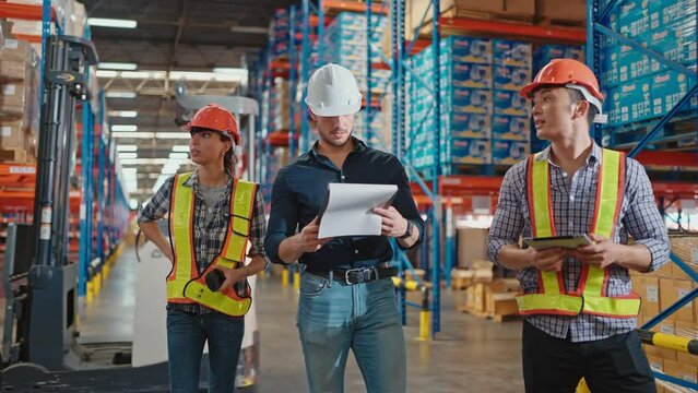 Businessman owner discussing with workers while walking through large warehouse distribution center in shelves with goods background. Logistic industry concept.