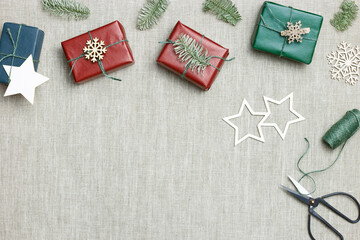 Christmas handmade gift boxes on textile background, craft paper wrapped presents with jute string, Christmas or New Year colors gifts. Top view set handcrafted gifts for holidays, eco style